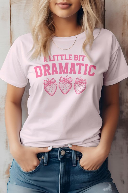 Person wearing a Vintage Coquette Strawberry Graphic Tee, featuring the text "A Little Bit Dramatic" and three illustrated strawberries below it, stands with hands in jean pockets. This stylish Bella Canvas tee is crafted from eco-friendly materials for a sustainable fashion choice.