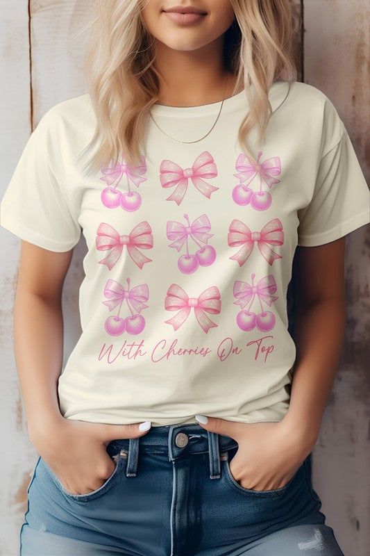 A person is standing with hands in their jean pockets, wearing a Vintage Coquette Cherry Graphic Tee that showcases a charming design of pink ribbons and cherries along with the text "With Cherries On Top.