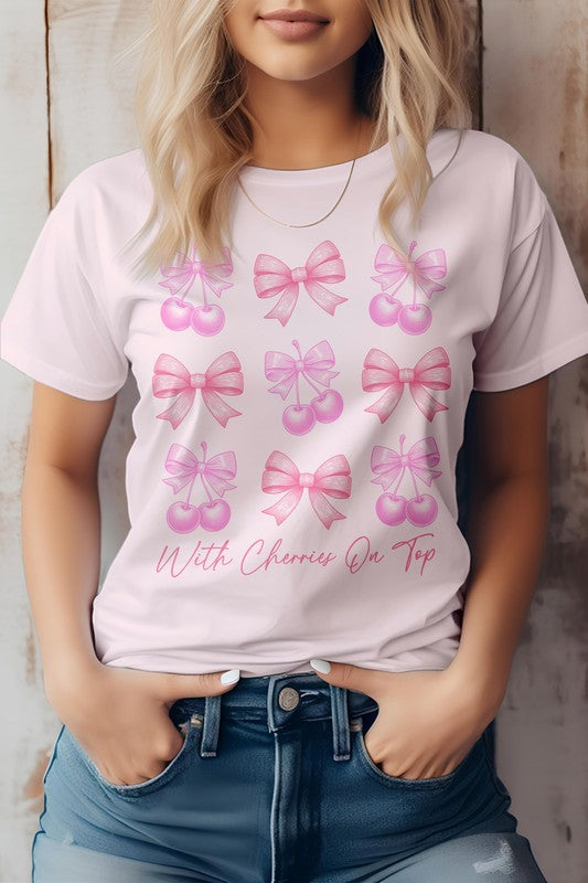 A person is standing with hands in their jean pockets, wearing a Vintage Coquette Cherry Graphic Tee that showcases a charming design of pink ribbons and cherries along with the text "With Cherries On Top.