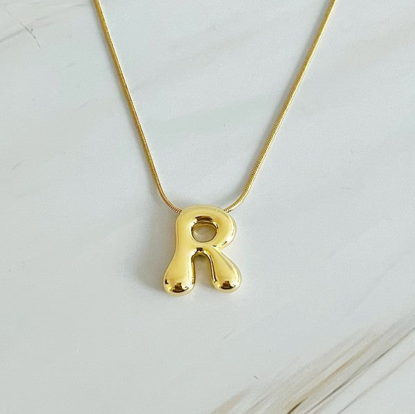 Gold necklaces featuring distinctive, balloon-shaped pendants of the letters E, N, K, L, M, and T against a white backdrop. These Balloon Letter Initial Necklaces are trend-setting and crafted in 18k gold plating for a stylish complement to any ensemble.