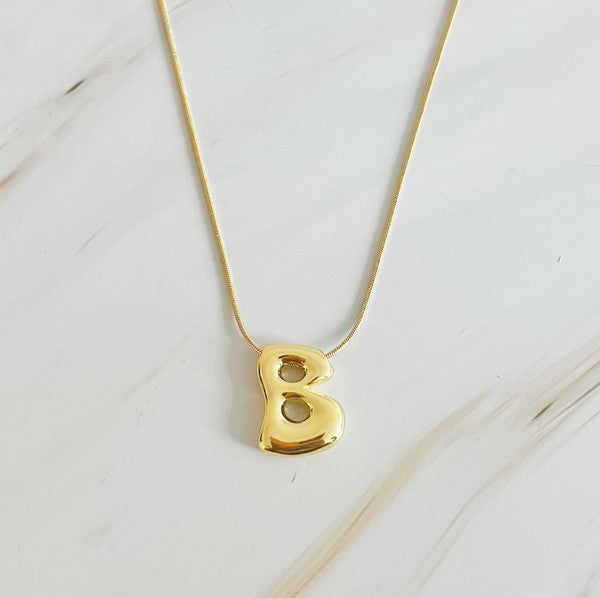 Gold necklaces featuring distinctive, balloon-shaped pendants of the letters E, N, K, L, M, and T against a white backdrop. These Balloon Letter Initial Necklaces are trend-setting and crafted in 18k gold plating for a stylish complement to any ensemble.