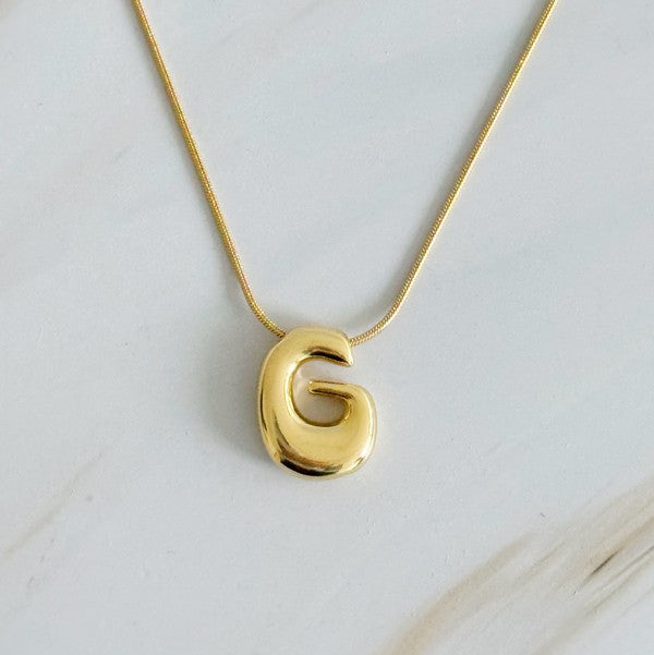 Gold necklaces featuring distinctive, balloon-shaped pendants of the letters E, N, K, L, M, and T against a white backdrop. These Balloon Letter Initial Necklaces are trend-setting and crafted in 18k gold plating for a stylish complement to any ensemble.