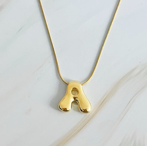 Gold necklaces featuring distinctive, balloon-shaped pendants of the letters E, N, K, L, M, and T against a white backdrop. These Balloon Letter Initial Necklaces are trend-setting and crafted in 18k gold plating for a stylish complement to any ensemble.