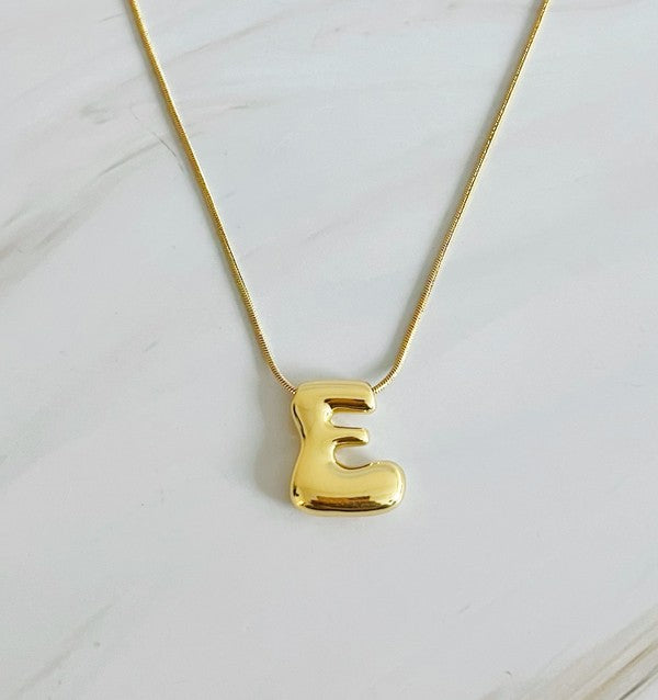 Gold necklaces featuring distinctive, balloon-shaped pendants of the letters E, N, K, L, M, and T against a white backdrop. These Balloon Letter Initial Necklaces are trend-setting and crafted in 18k gold plating for a stylish complement to any ensemble.