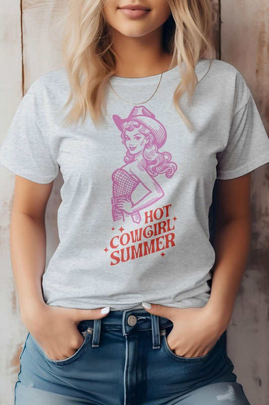 A person wearing the "Hot Cowgirl Summer" Retro Western Graphic Tee, which features an illustrated cowgirl and the text "Hot Cowgirl Summer." They have their hands in the pockets of their denim shorts, highlighting a stylish look made from eco-friendly materials.