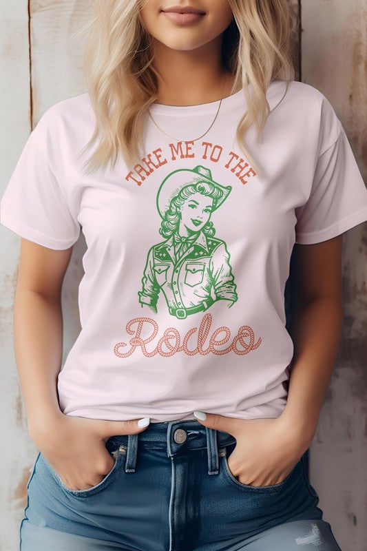 A woman is wearing the "Take Me To The Rodeo, Retro Western Graphic Tee," a light green shirt featuring a vintage-style cowgirl graphic and the text "TAKE ME TO THE RODEO," made from eco-friendly materials, with her hands in jean pockets.