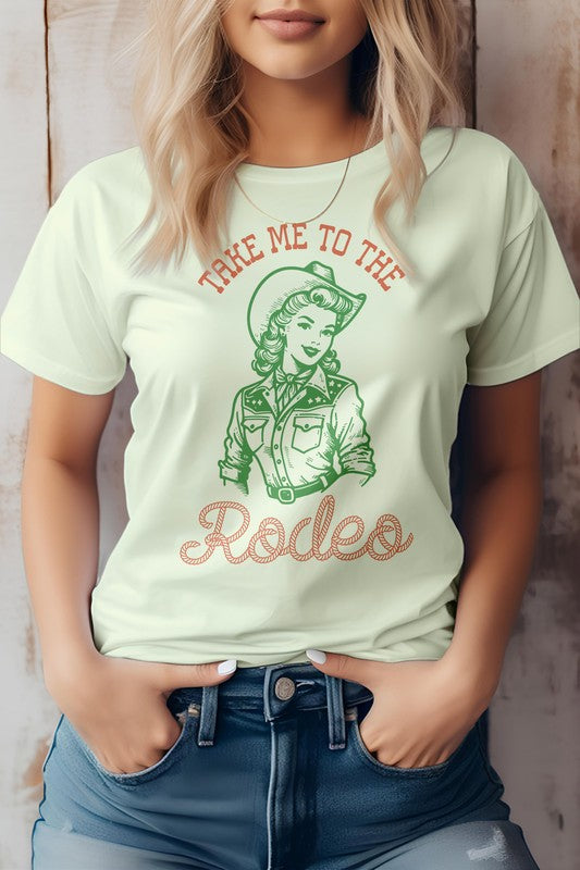 A woman is wearing the "Take Me To The Rodeo, Retro Western Graphic Tee," a light green shirt featuring a vintage-style cowgirl graphic and the text "TAKE ME TO THE RODEO," made from eco-friendly materials, with her hands in jean pockets.