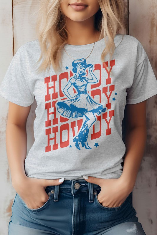 Woman wearing a light gray "Howdy Howdy Howdy, Retro Western Graphic Tee" featuring a cowgirl illustration, paired with denim shorts.