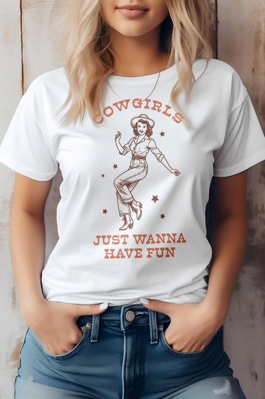 A person wearing the "Cowgirls Just Wanna Have Fun, Western Graphic Tee" featuring a retro illustration of a cowgirl and the caption "Cowgirls just wanna have fun," standing against a neutral background.