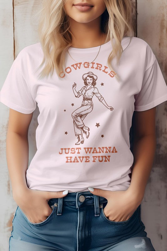 A person wearing the "Cowgirls Just Wanna Have Fun, Western Graphic Tee" featuring a retro illustration of a cowgirl and the caption "Cowgirls just wanna have fun," standing against a neutral background.