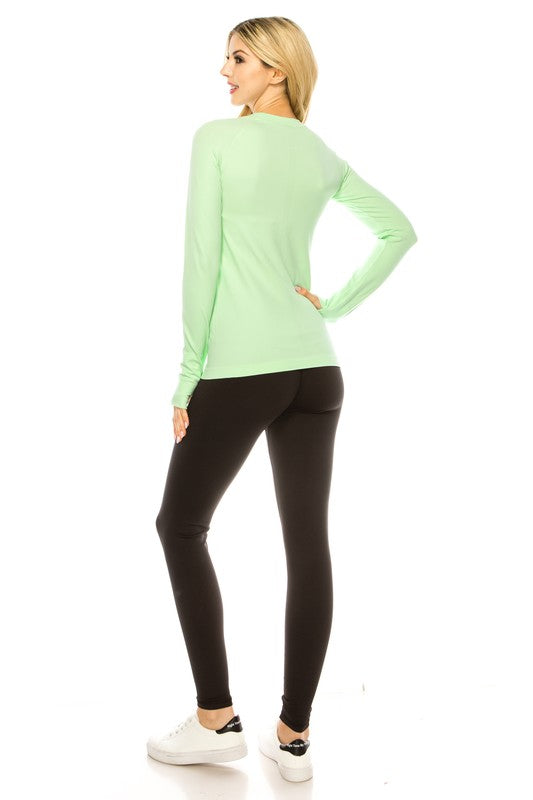 A person is standing in a bright yellow Long Sleeve Workout Shirt for Women, paired with black leggings and white sneakers, posing against a white background. This outfit perfectly showcases stylish athletic wear.