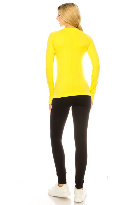 A person is standing in a bright yellow Long Sleeve Workout Shirt for Women, paired with black leggings and white sneakers, posing against a white background. This outfit perfectly showcases stylish athletic wear.