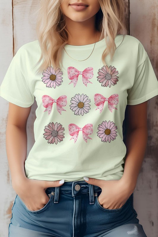 A person wearing a light pink Coquette Pink Bow Daisy Flower Boho Graphic Tee, which showcases alternating flowers and pink bows. They have their hands in the pockets of their blue jeans.