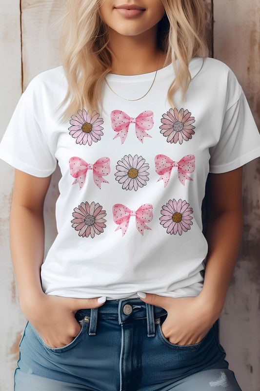 A person wearing a light pink Coquette Pink Bow Daisy Flower Boho Graphic Tee, which showcases alternating flowers and pink bows. They have their hands in the pockets of their blue jeans.