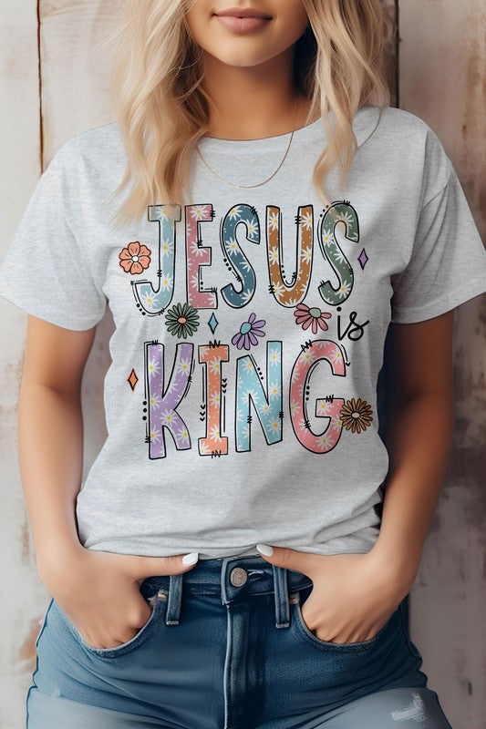 A person wearing the "Jesus is King, Christian Graphic Tee," a white t-shirt adorned with vibrant text and floral designs, crafted from superior combed cotton.