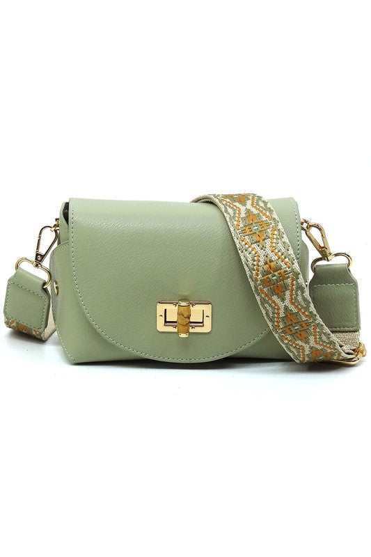 The Bamboo Twist Lock Flap Crossbody Bag is a small peach-colored bag made from faux vegan leather. It features a chic bamboo twist lock for added elegance, a gold clasp, and an adjustable patterned shoulder strap with black and brown geometric designs.