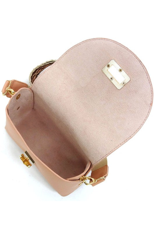 The Bamboo Twist Lock Flap Crossbody Bag is a small peach-colored bag made from faux vegan leather. It features a chic bamboo twist lock for added elegance, a gold clasp, and an adjustable patterned shoulder strap with black and brown geometric designs.