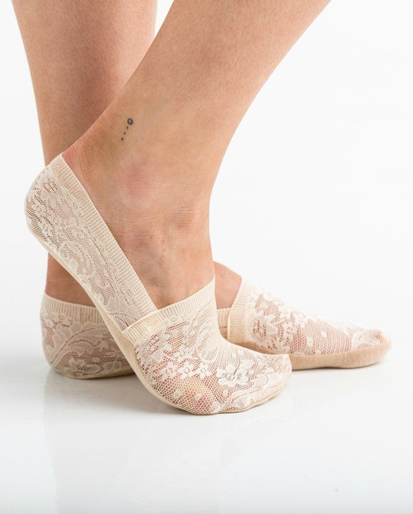 Wearing a pair from the No Slip Floral Lace Sneaker Socks- 3 Pack, her feet are stylishly clad in nude-colored no-show socks featuring a delicate floral lace pattern. A small ankle tattoo with three dots adds a personal touch, while the no-slip design ensures they stay perfectly in place.