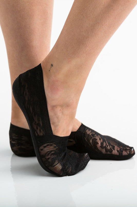 Wearing a pair from the No Slip Floral Lace Sneaker Socks- 3 Pack, her feet are stylishly clad in nude-colored no-show socks featuring a delicate floral lace pattern. A small ankle tattoo with three dots adds a personal touch, while the no-slip design ensures they stay perfectly in place.