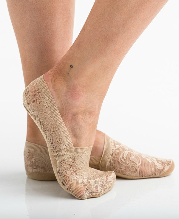 Wearing a pair from the No Slip Floral Lace Sneaker Socks- 3 Pack, her feet are stylishly clad in nude-colored no-show socks featuring a delicate floral lace pattern. A small ankle tattoo with three dots adds a personal touch, while the no-slip design ensures they stay perfectly in place.