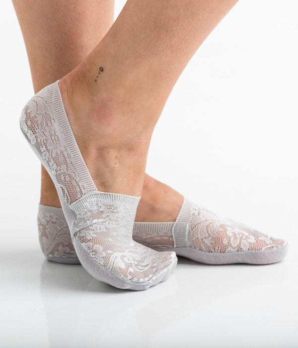 Wearing a pair from the No Slip Floral Lace Sneaker Socks- 3 Pack, her feet are stylishly clad in nude-colored no-show socks featuring a delicate floral lace pattern. A small ankle tattoo with three dots adds a personal touch, while the no-slip design ensures they stay perfectly in place.