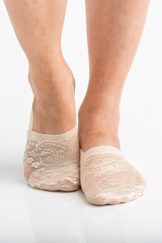 Wearing a pair from the No Slip Floral Lace Sneaker Socks- 3 Pack, her feet are stylishly clad in nude-colored no-show socks featuring a delicate floral lace pattern. A small ankle tattoo with three dots adds a personal touch, while the no-slip design ensures they stay perfectly in place.