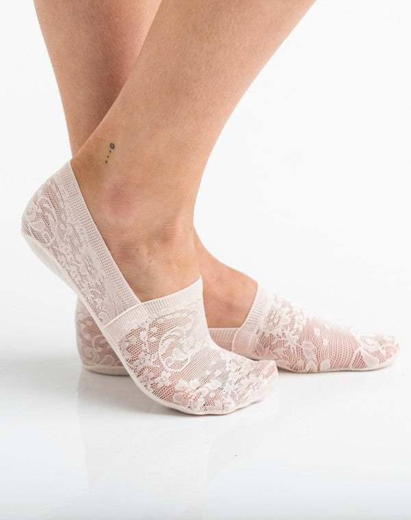 Wearing a pair from the No Slip Floral Lace Sneaker Socks- 3 Pack, her feet are stylishly clad in nude-colored no-show socks featuring a delicate floral lace pattern. A small ankle tattoo with three dots adds a personal touch, while the no-slip design ensures they stay perfectly in place.