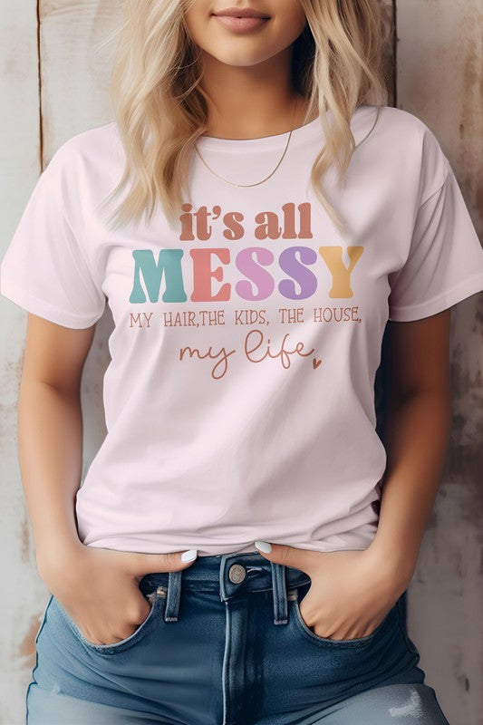 A person wearing a white "Mama Mom Mother's Day Graphic Tee" featuring the text "It's all messy my hair, the kids, the house, my life." The T-shirt is paired with blue jeans.