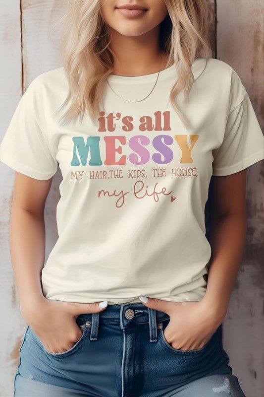 A person wearing a white "Mama Mom Mother's Day Graphic Tee" featuring the text "It's all messy my hair, the kids, the house, my life." The T-shirt is paired with blue jeans.