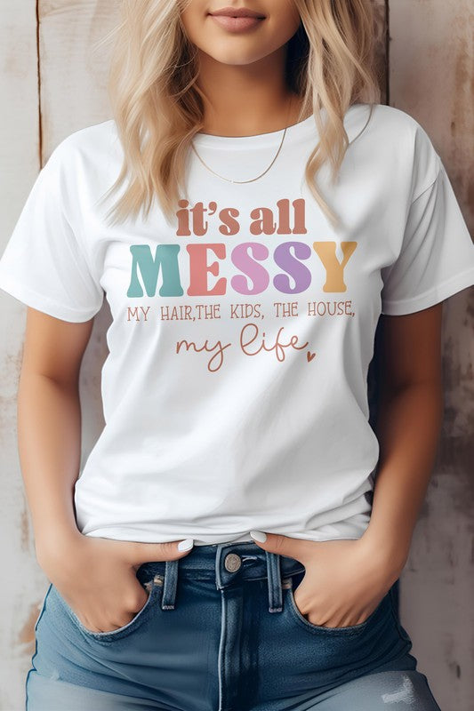 A person wearing a white "Mama Mom Mother's Day Graphic Tee" featuring the text "It's all messy my hair, the kids, the house, my life." The T-shirt is paired with blue jeans.