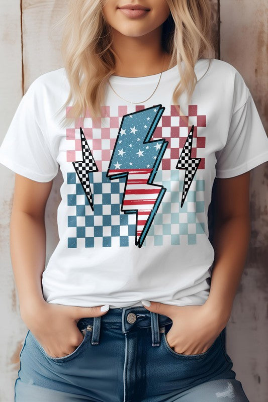 Person wearing the America Flag Lightning Bolt Checker Graphic Tee, a white t-shirt with a lightning bolt overlaying a red, white, and blue checkered pattern—perfect for celebrating the 4th of July. Hands are in the front pockets of blue jeans.