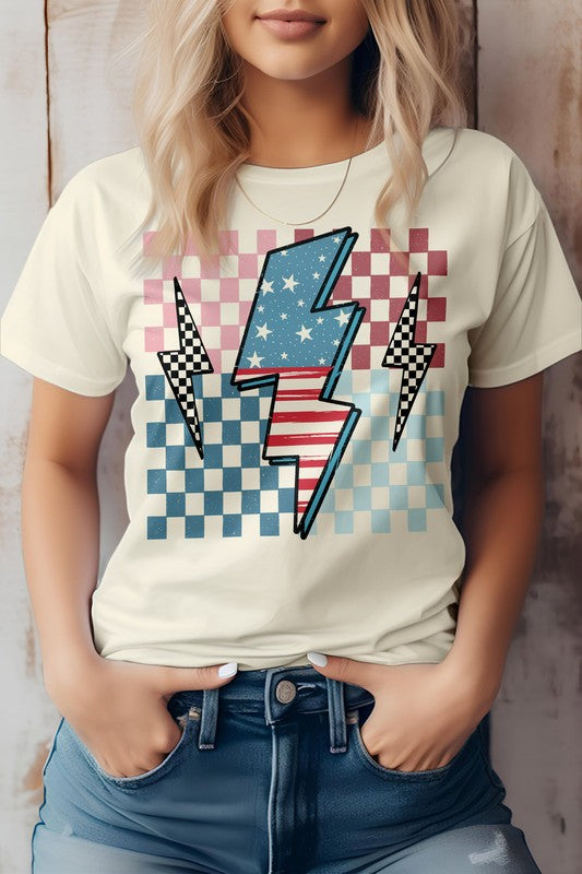 Person wearing the America Flag Lightning Bolt Checker Graphic Tee, a white t-shirt with a lightning bolt overlaying a red, white, and blue checkered pattern—perfect for celebrating the 4th of July. Hands are in the front pockets of blue jeans.