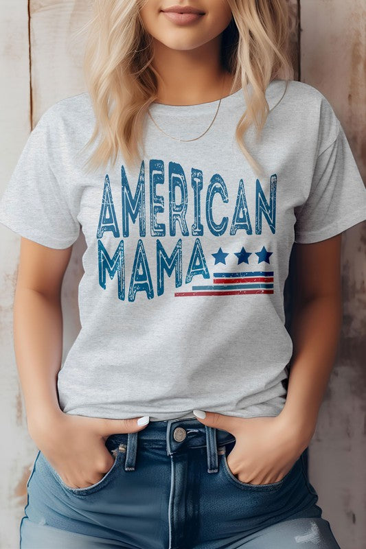 A person wearing an eco-friendly American Mama Retro 4th of July Graphic Tee, featuring a beige background with the text "American Mama" and a design of stars and stripes, stands with hands in their pockets, embodying the spirit of the 4th of July.