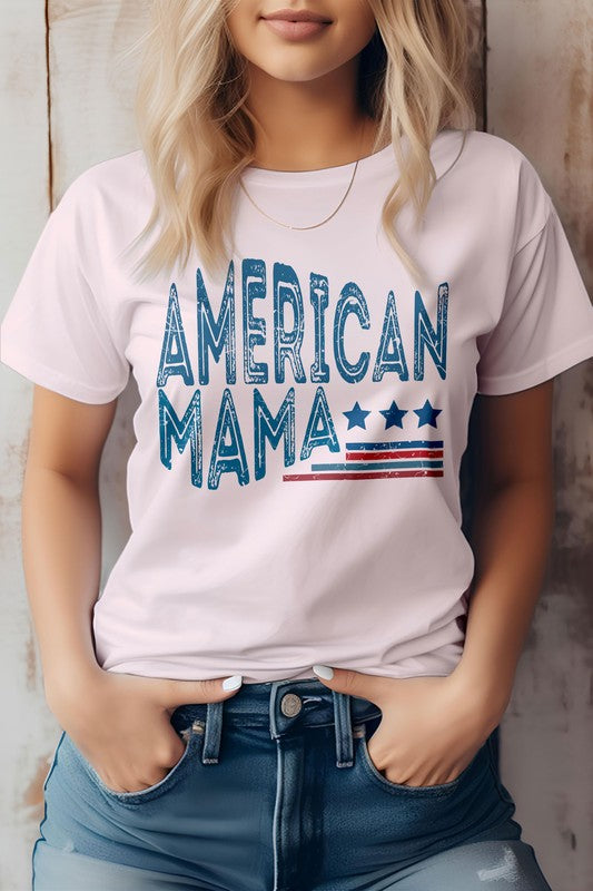 A person wearing an eco-friendly American Mama Retro 4th of July Graphic Tee, featuring a beige background with the text "American Mama" and a design of stars and stripes, stands with hands in their pockets, embodying the spirit of the 4th of July.