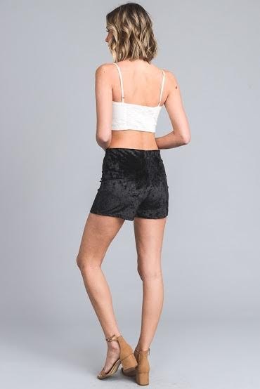 A person wearing black, stretch velvet Shorts with a lace-up front detail and beige open-toe heels. The upper body is partially visible.