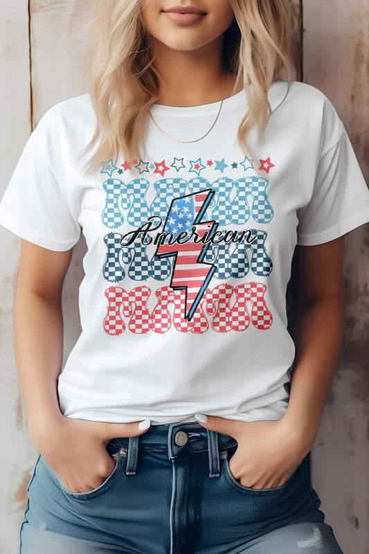 A person wearing the "American Mama Retro" graphic tee, featuring blue and red checkered letters with a lightning bolt design, tucked into jeans.