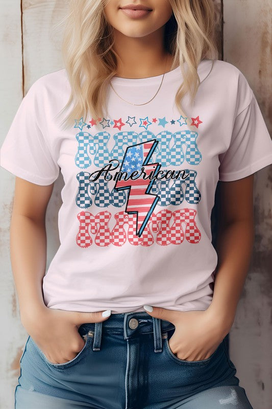 A person wearing the "American Mama Retro" graphic tee, featuring blue and red checkered letters with a lightning bolt design, tucked into jeans.