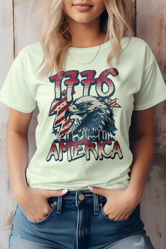 Against a wooden backdrop, an individual wears the 1776 America 4th of July Oversized Tee, crafted from eco-friendly materials. This shirt features "1776" and an eagle graphic with the word "America," perfectly capturing the patriotic spirit of Independence Day.