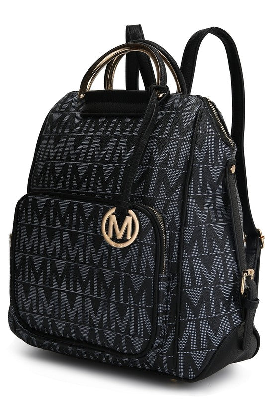 A person wearing a light-colored jacket and floral skirt is carrying the MKF Collection Cora Milan Backpack by Mia K, which features a blue pattern with metallic accents, an 'M' logo, and an adjustable shoulder strap.