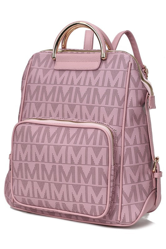 A person wearing a light-colored jacket and floral skirt is carrying the MKF Collection Cora Milan Backpack by Mia K, which features a blue pattern with metallic accents, an 'M' logo, and an adjustable shoulder strap.