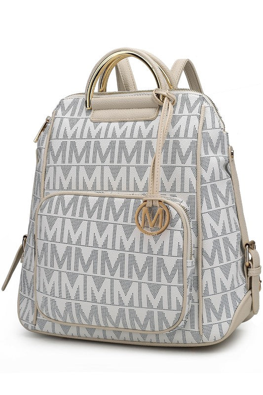 A person wearing a light-colored jacket and floral skirt is carrying the MKF Collection Cora Milan Backpack by Mia K, which features a blue pattern with metallic accents, an 'M' logo, and an adjustable shoulder strap.