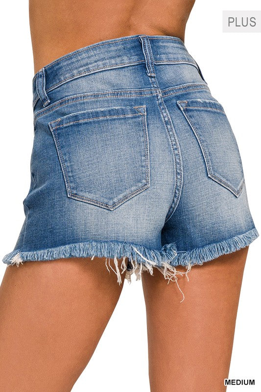 Close-up of a person wearing the Plus Mid Rise Raw Frayed Hem Denim Shorts, crafted from stretch denim.