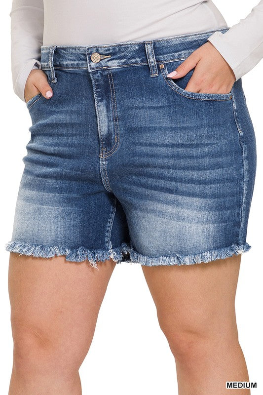 A person is wearing Zenana's Plus Mid Rise Raw Frayed Hem Denim Shorts in blue.