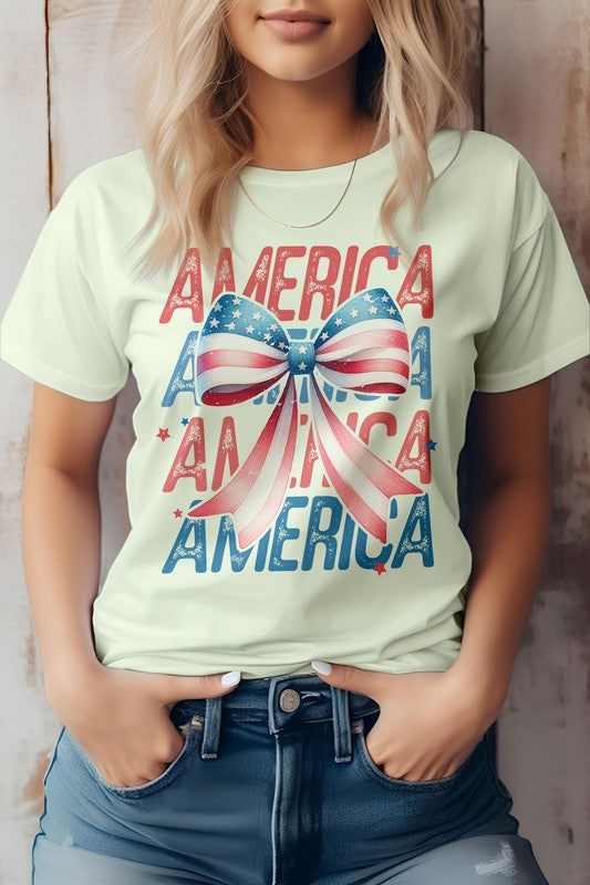 A person wearing the Patriotic Coquette Bow 4th of July Graphic Tee, which showcases the word "America" and a bow in red, white, and blue print, stands proudly, making it perfect for celebrating the 4th of July.