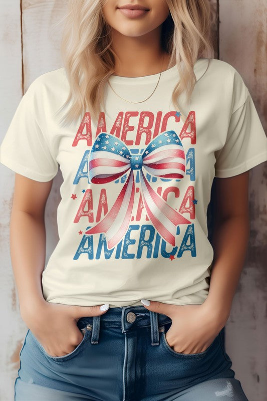 A person wearing the Patriotic Coquette Bow 4th of July Graphic Tee, which showcases the word "America" and a bow in red, white, and blue print, stands proudly, making it perfect for celebrating the 4th of July.