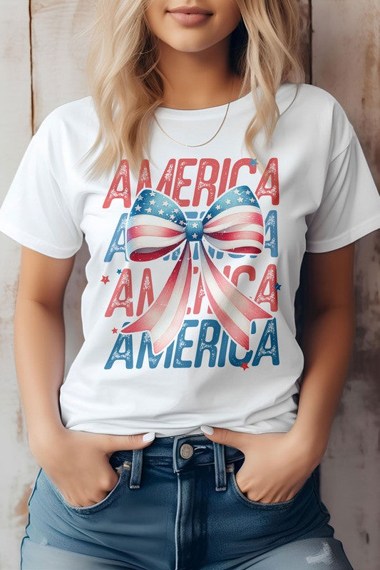 A person wearing the Patriotic Coquette Bow 4th of July Graphic Tee, which showcases the word "America" and a bow in red, white, and blue print, stands proudly, making it perfect for celebrating the 4th of July.