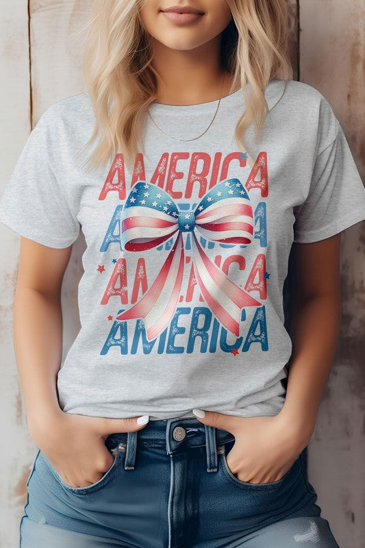 A person wearing the Patriotic Coquette Bow 4th of July Graphic Tee, which showcases the word "America" and a bow in red, white, and blue print, stands proudly, making it perfect for celebrating the 4th of July.