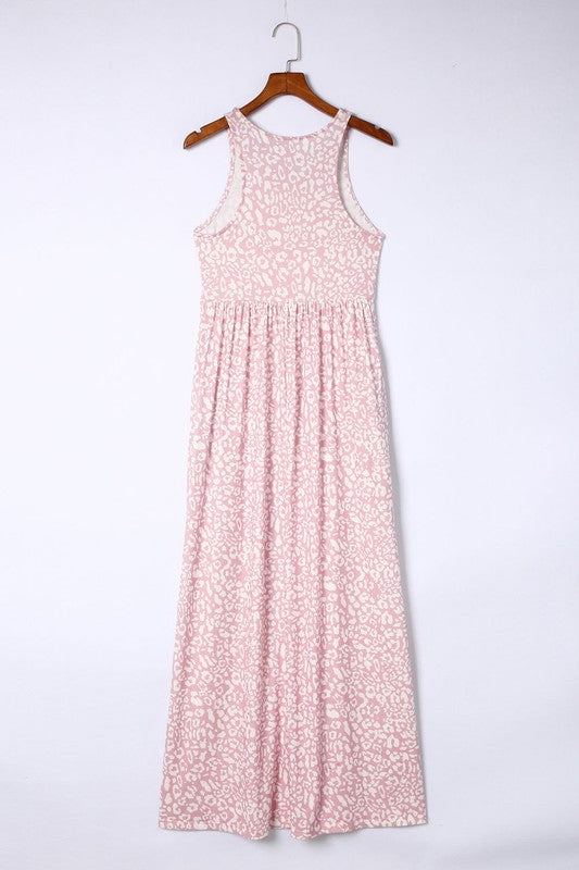 The Leopard Dust Baby Pink Sleeveless Maxi Dress, featuring a stylish white leopard print design on soft polyester fabric, elegantly drapes over a wooden hanger against a pristine white backdrop.