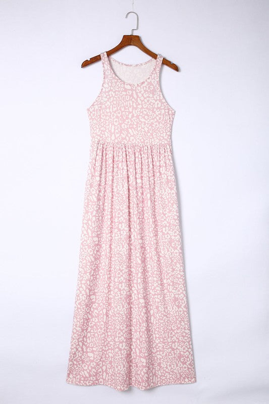 The Leopard Dust Baby Pink Sleeveless Maxi Dress, featuring a stylish white leopard print design on soft polyester fabric, elegantly drapes over a wooden hanger against a pristine white backdrop.