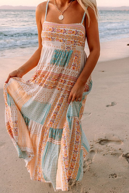 A Patchwork mint coral long sundress, featuring a Bohemian-inspired colorful patchwork print, sleeveless design with spaghetti straps and a square neckline, along with an A-line silhouette, is hanging on a wooden hanger against a plain white background.